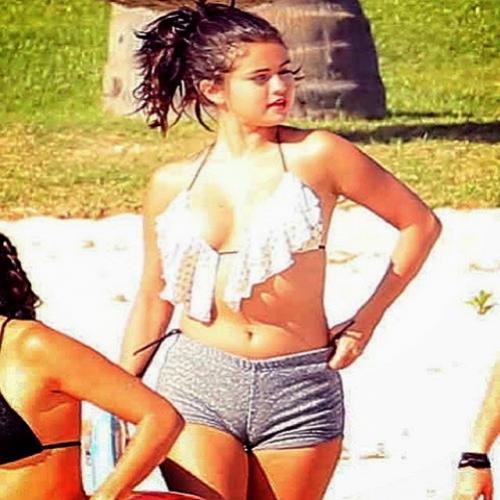 Selena Gomez com biquíni decotado e shortinho molhado na praia.